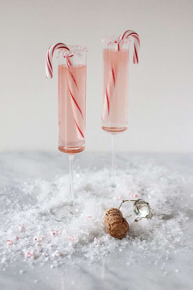 two champagne flutes with candy canes in them sitting on top of snow covered ground