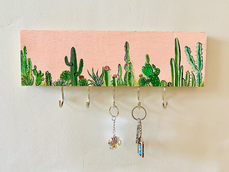 three key hooks hanging from a wall with cactus designs on them and dangling from the hooks