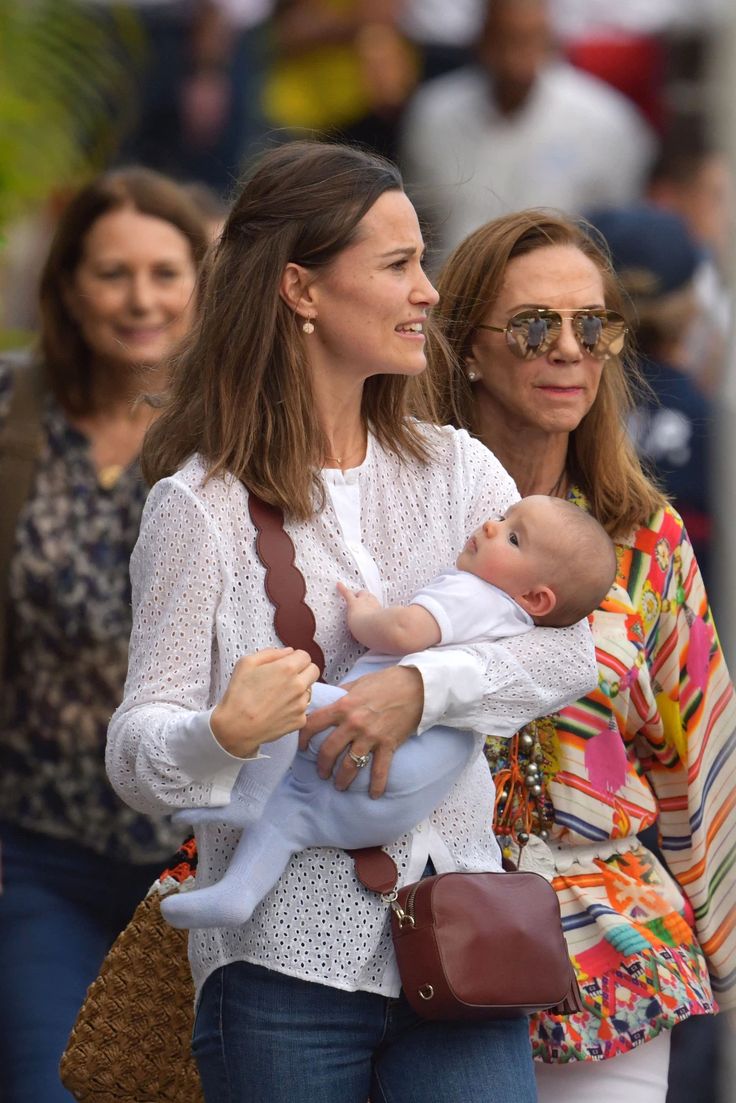 two women are walking with a baby in their arms and one woman is holding a purse