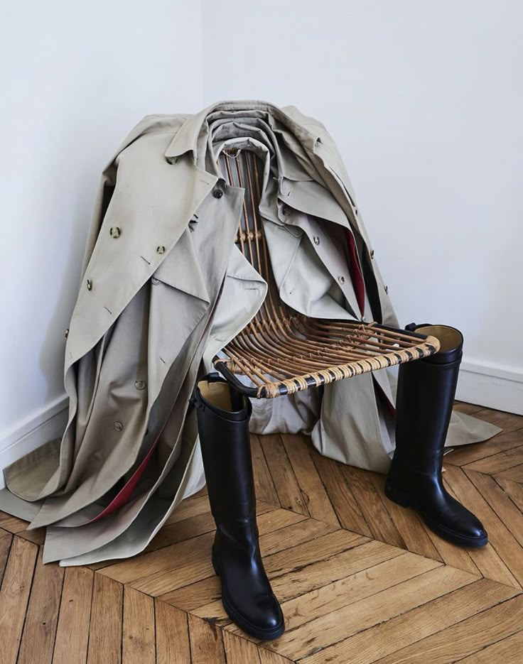 a pair of black boots sitting on top of a wooden bench next to a trench coat