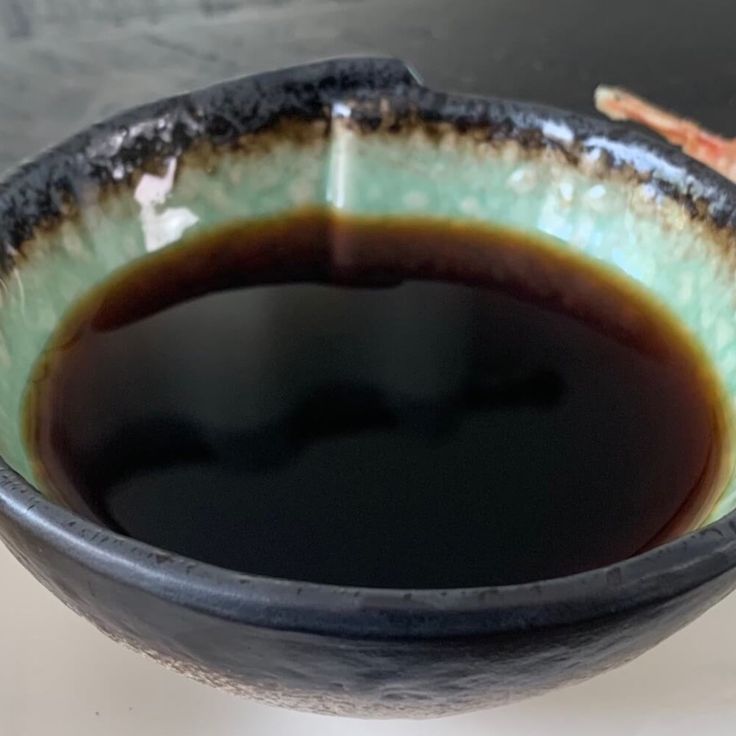 a black and green bowl filled with brown liquid on top of a white countertop