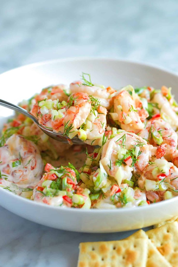 a white bowl filled with shrimp salad next to crackers