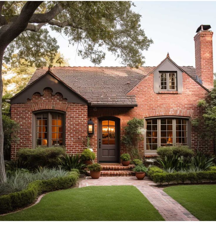 a brick house with lots of windows and plants around it's front door, surrounded by greenery