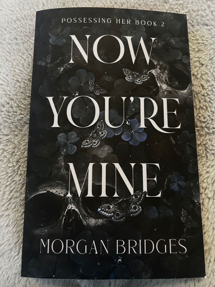 the book now you're mine by morgan bridges is laying on a white carpet