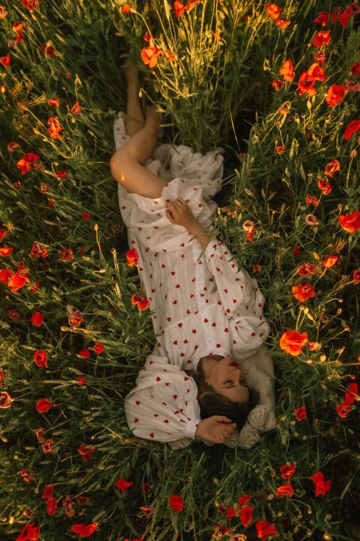 a woman laying in the grass with red flowers