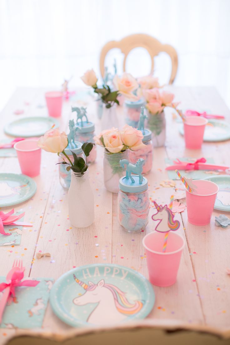 the table is set with pink and blue plates, cups, and vases on it