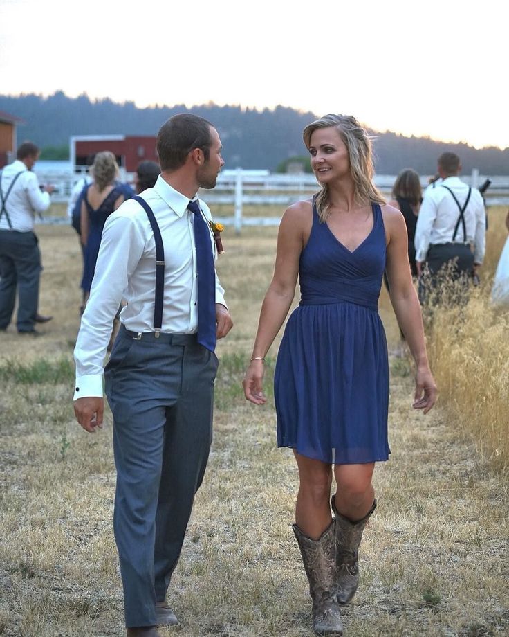 a man and woman walking through a field holding hands with other people in the background