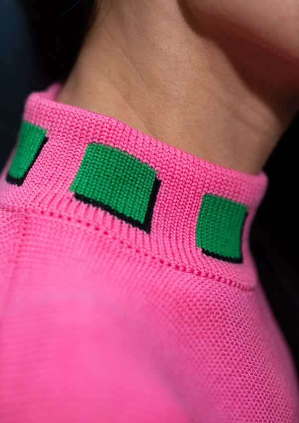 a woman wearing a pink sweater with green squares on it