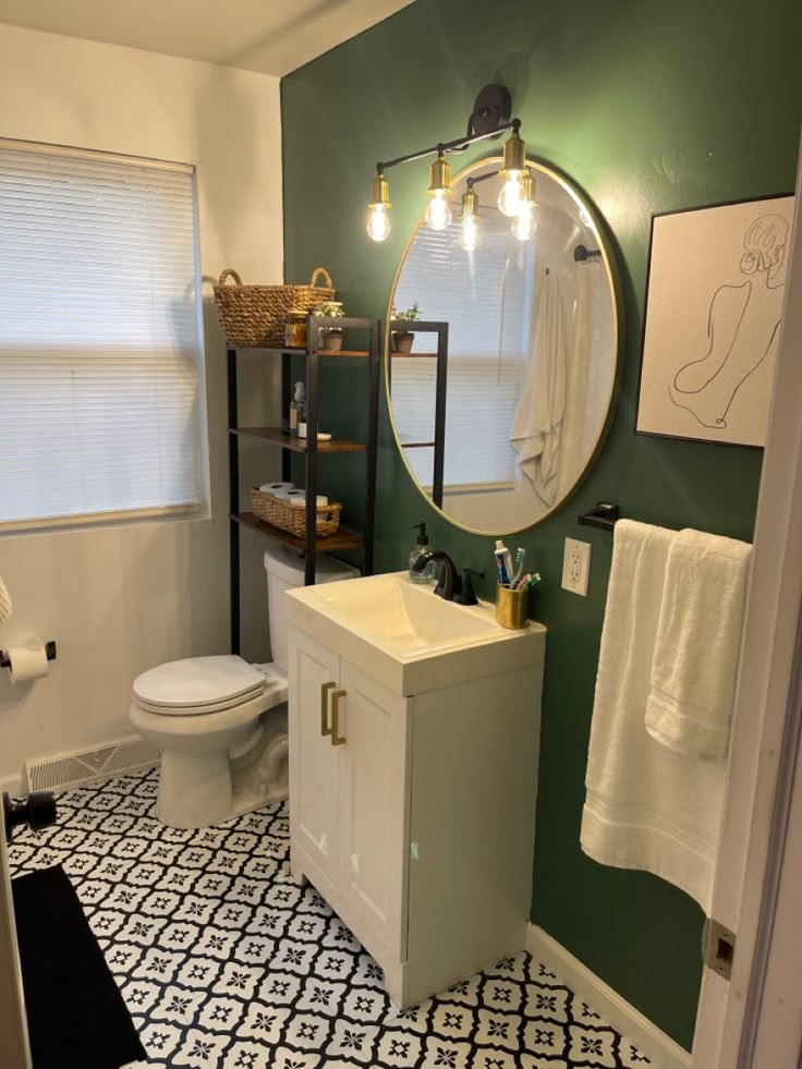 a bathroom with green walls and black and white flooring, including a round mirror above the sink