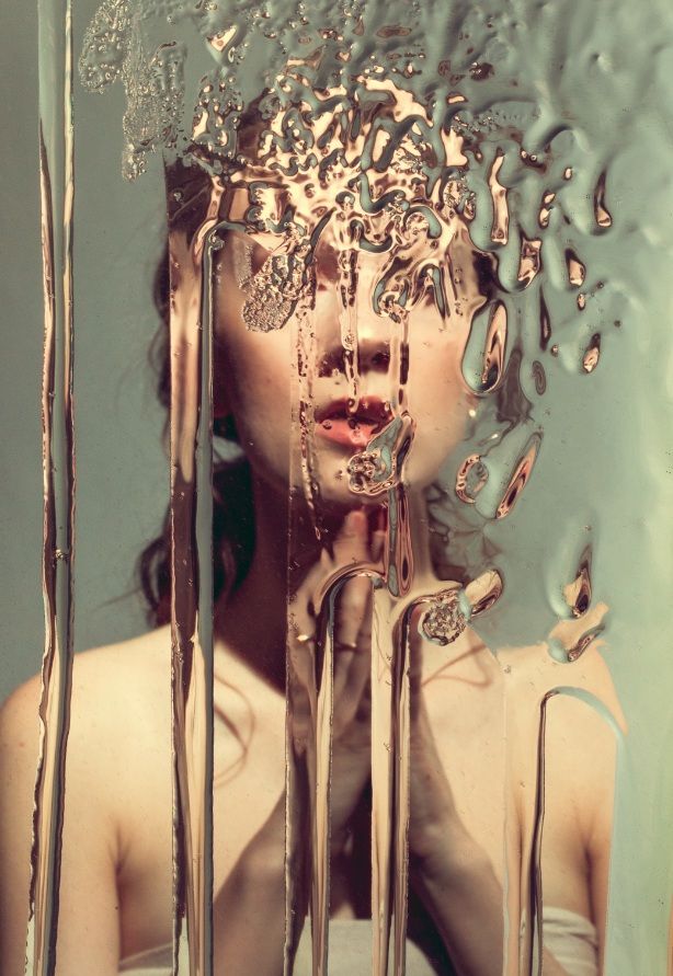 a woman's face is reflected in a mirror with water dripping on it and her hair blowing back