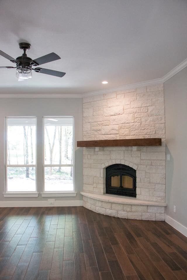 an empty living room with wood floors and a ceiling fan in the corner, next to a fireplace