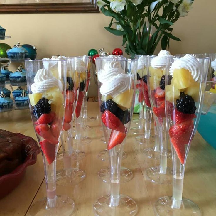 there are many desserts in wine glasses on the table, including strawberries and bananas