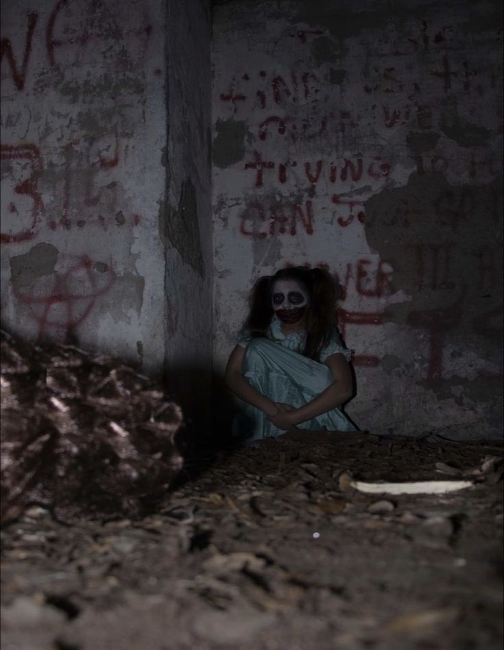 a woman with makeup on her face sitting in an old room next to a large rock