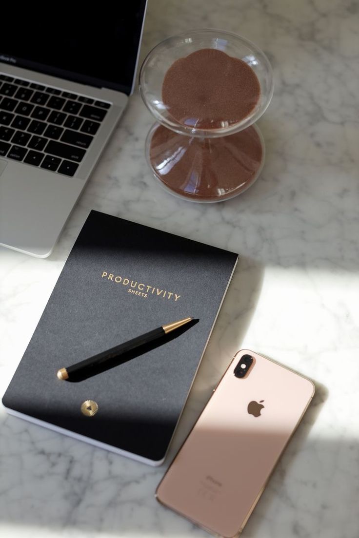 an iphone, notebook and pen sitting on a marble table next to a laptop computer