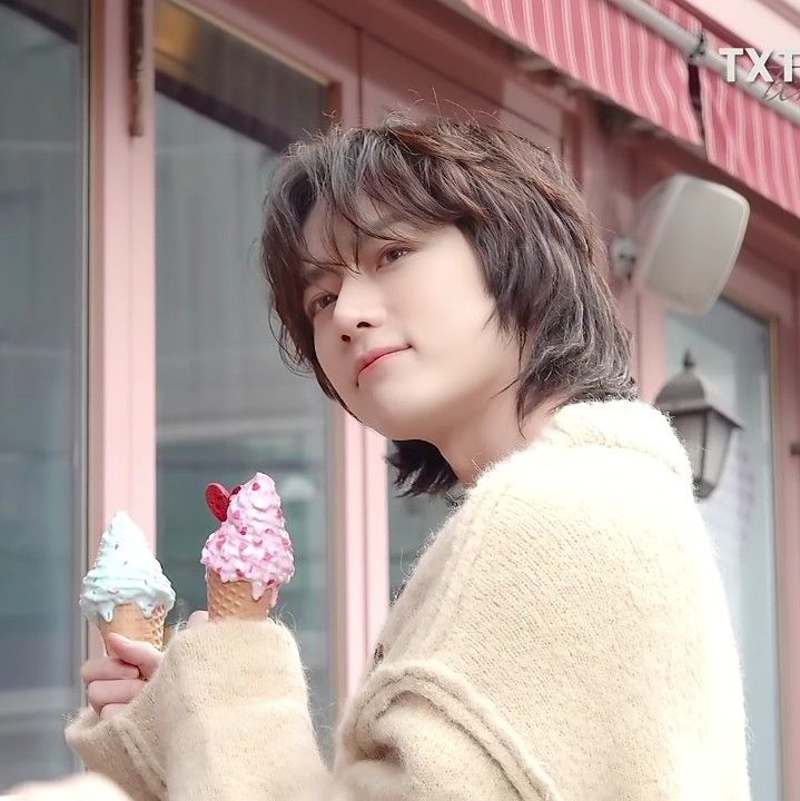 a person holding an ice cream cone in front of a building with pink and blue icing on it