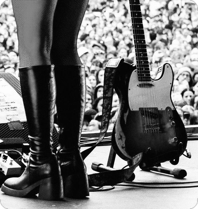 black and white photograph of woman's legs in high heel boots with guitar on stage