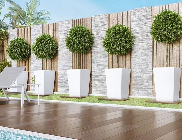 there is a white chair next to a wall with potted plants on it and a pool in the foreground