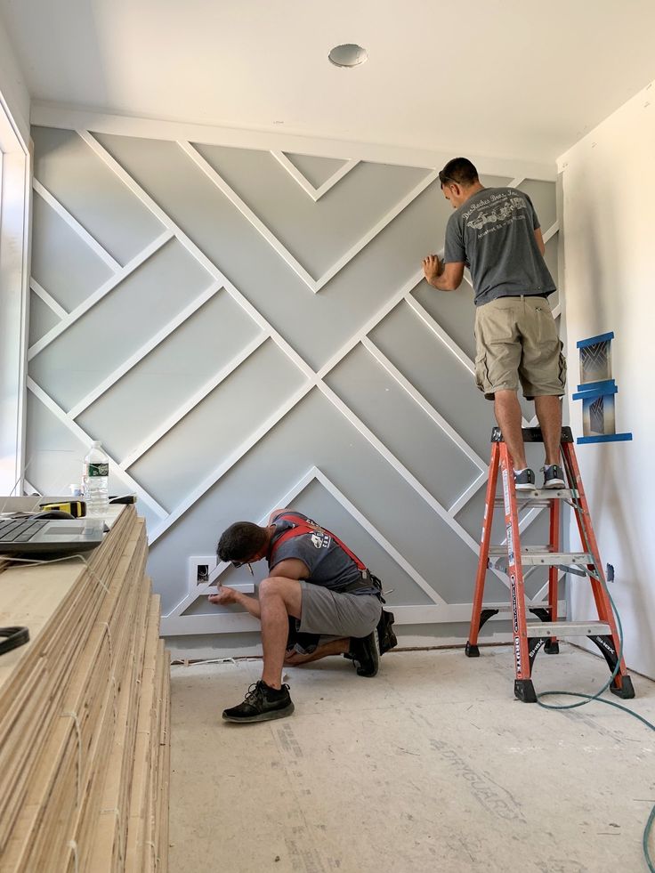 two men working on a wall in a room that has been painted gray and white