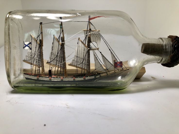 a ship in a bottle on a white surface with no people around it and the bottom half is empty