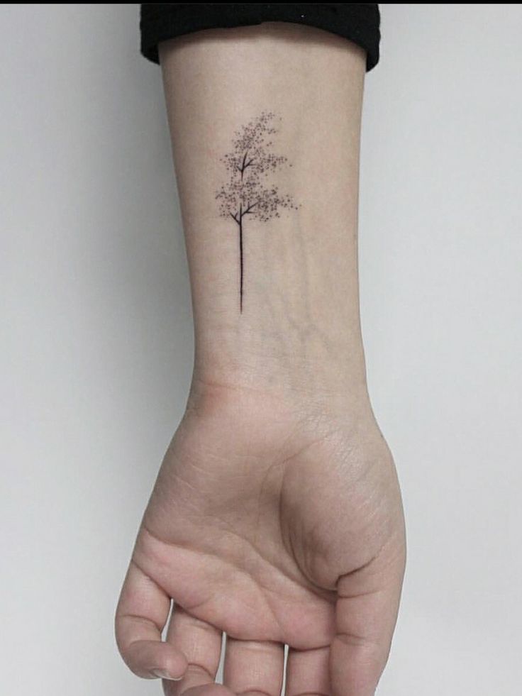 a small tree tattoo on the wrist is shown in black ink, and it appears to be tiny