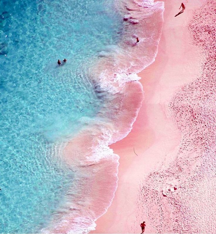 two people are swimming in the blue and pink water on a beach with white sand