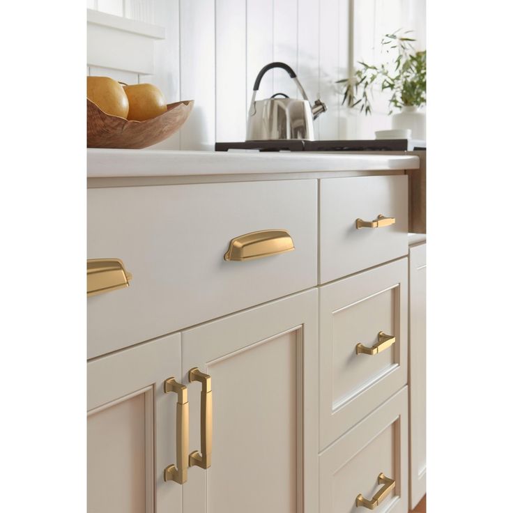 a kitchen with white cabinets and gold pulls on the handles, along with a bowl of fruit