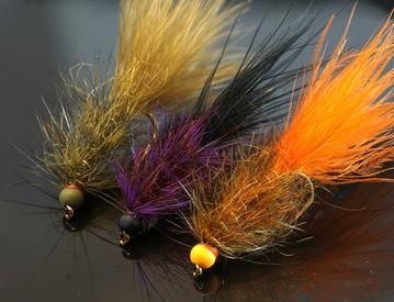 three different colored flies sitting on top of a black table next to orange and yellow feathers