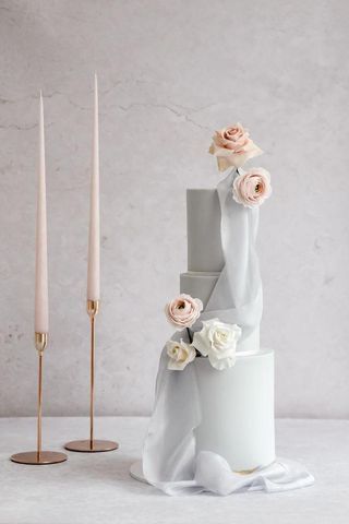 a three tiered wedding cake with flowers on top and two candles in the background