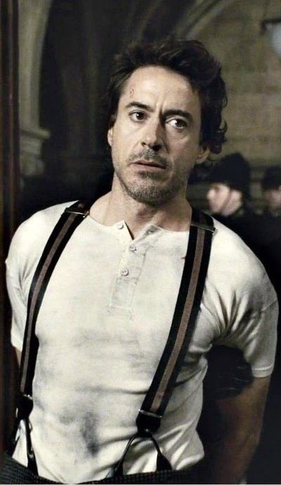 a man with suspenders and a white t - shirt is looking at the camera