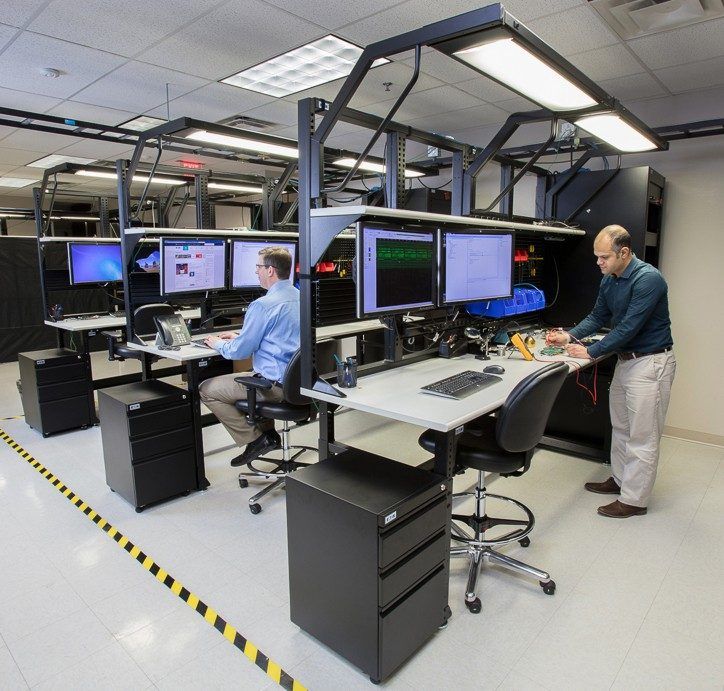 two men are standing in front of multiple computer monitors and desks with computers on them