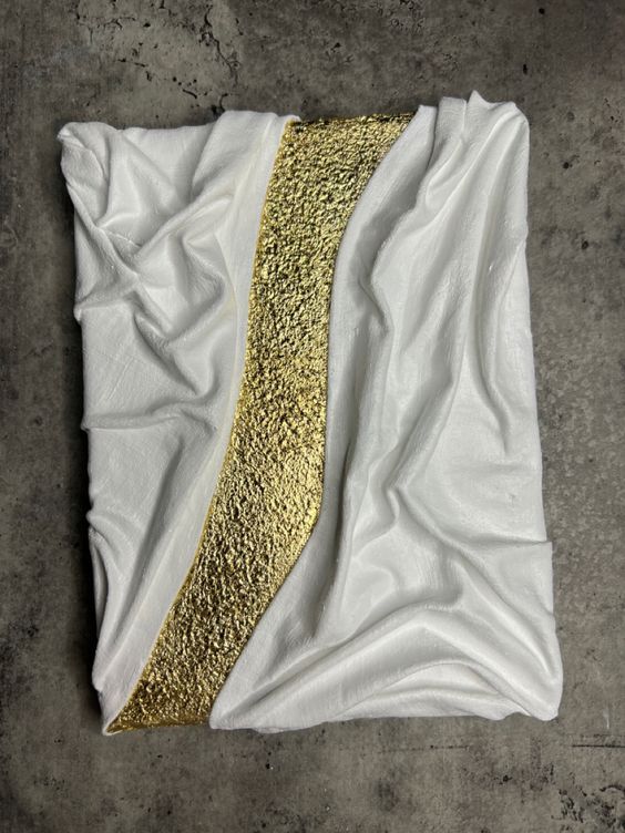 a piece of white and gold paper on the ground with some sort of material in it