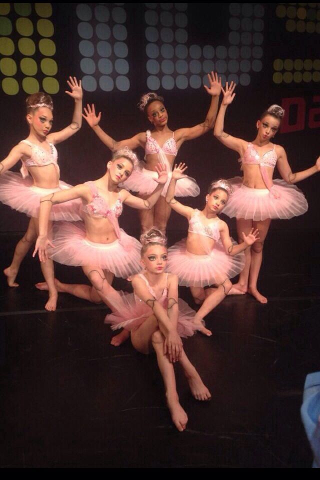 a group of young ballerinas posing for a photo on stage with their hands in the air