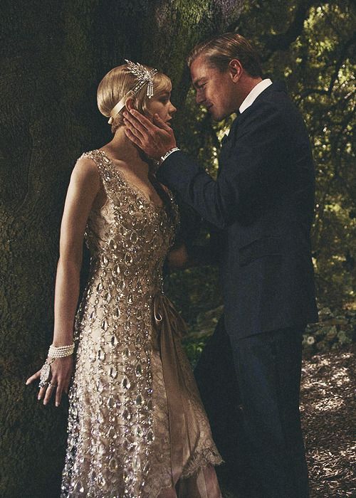 a man and woman standing next to each other in front of some trees with their hands together