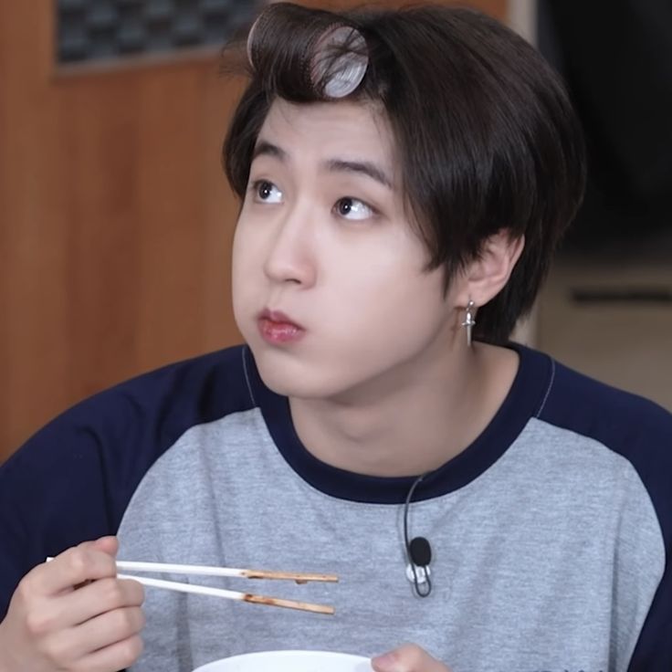 a young man holding chopsticks in his mouth while eating from a white bowl