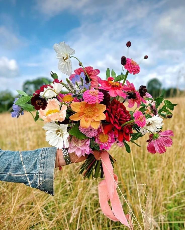 a person holding a bouquet of flowers in their hand on top of a grass field