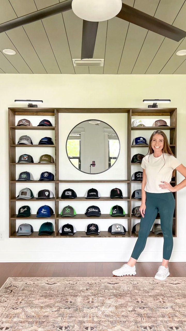 a woman is standing in front of a wall full of hats on shelves and shelving