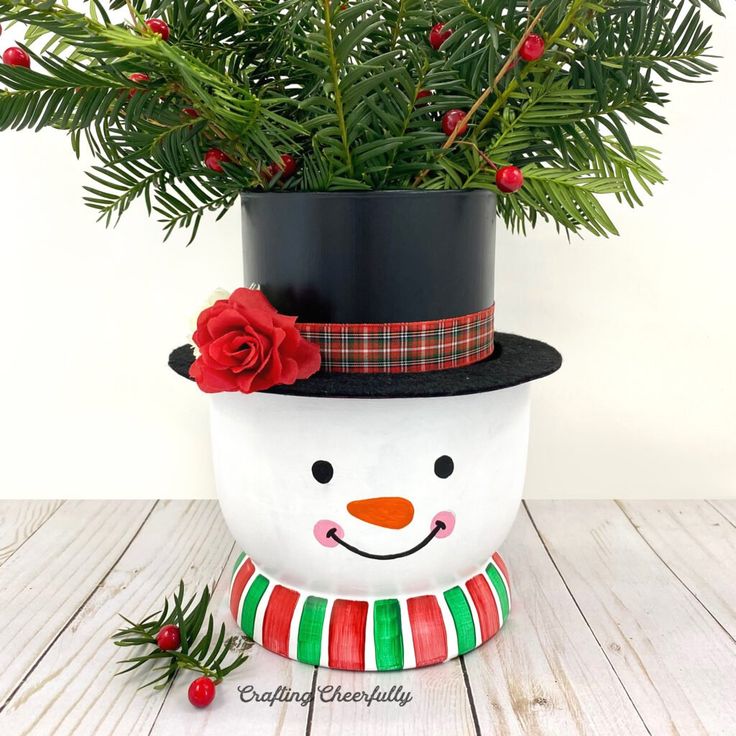 a potted plant with a snowman's hat on it and holly branches in the background