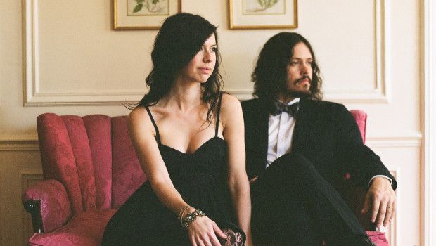 a man and woman in formal wear sitting on a pink couch next to each other