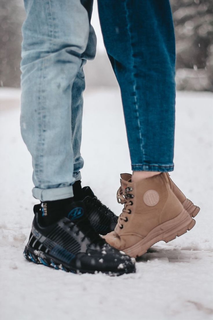 two people standing next to each other in the snow wearing winter boots and blue jeans