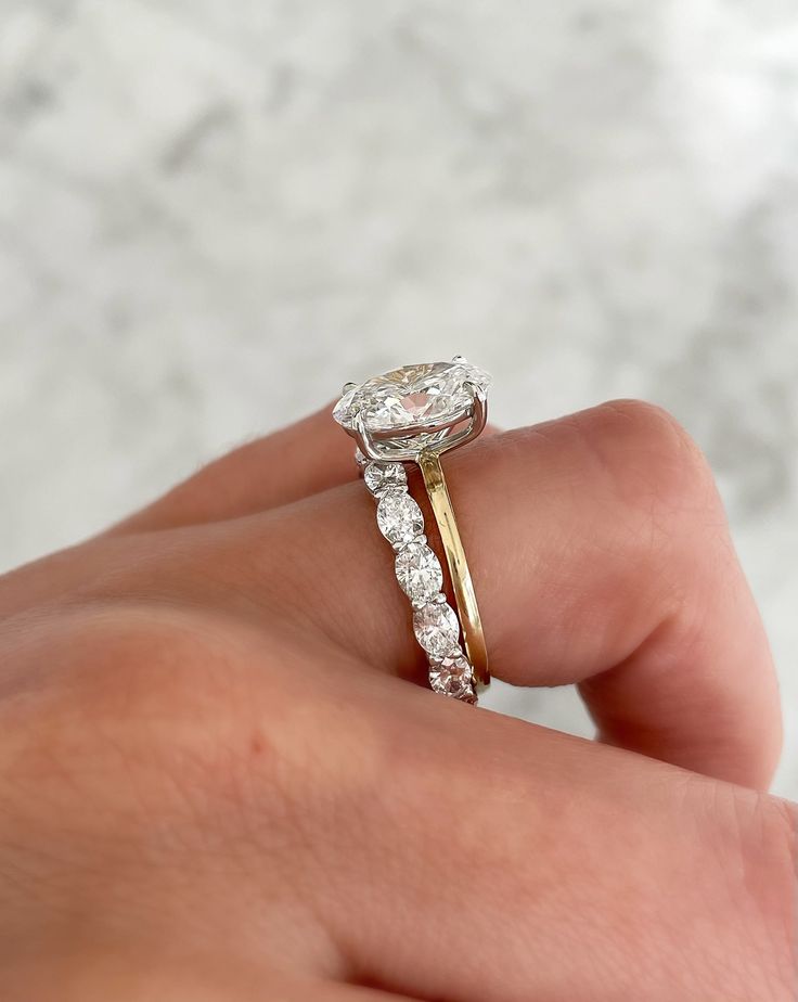 a woman's hand holding a ring with a diamond on it and two bands around the band