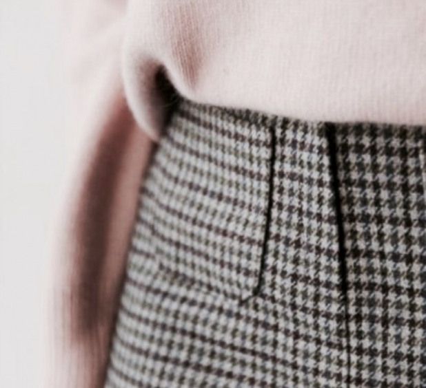 a close up of a person wearing a pink sweater and checkered skirt with buttons on the side