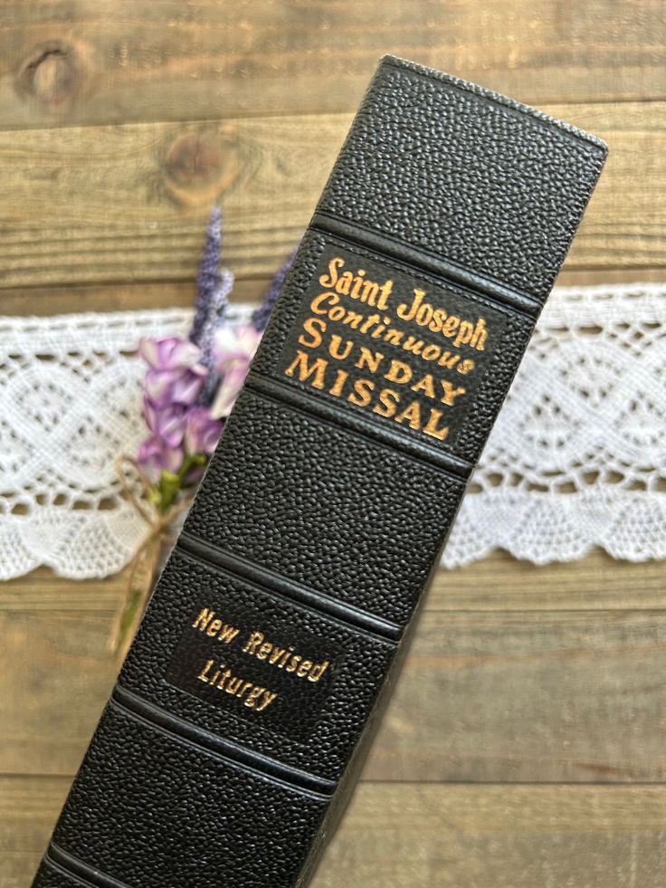 a black book sitting on top of a wooden table next to a purple and white flower