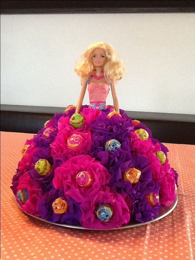 a barbie doll sitting on top of a purple and pink flowered cake with buttons