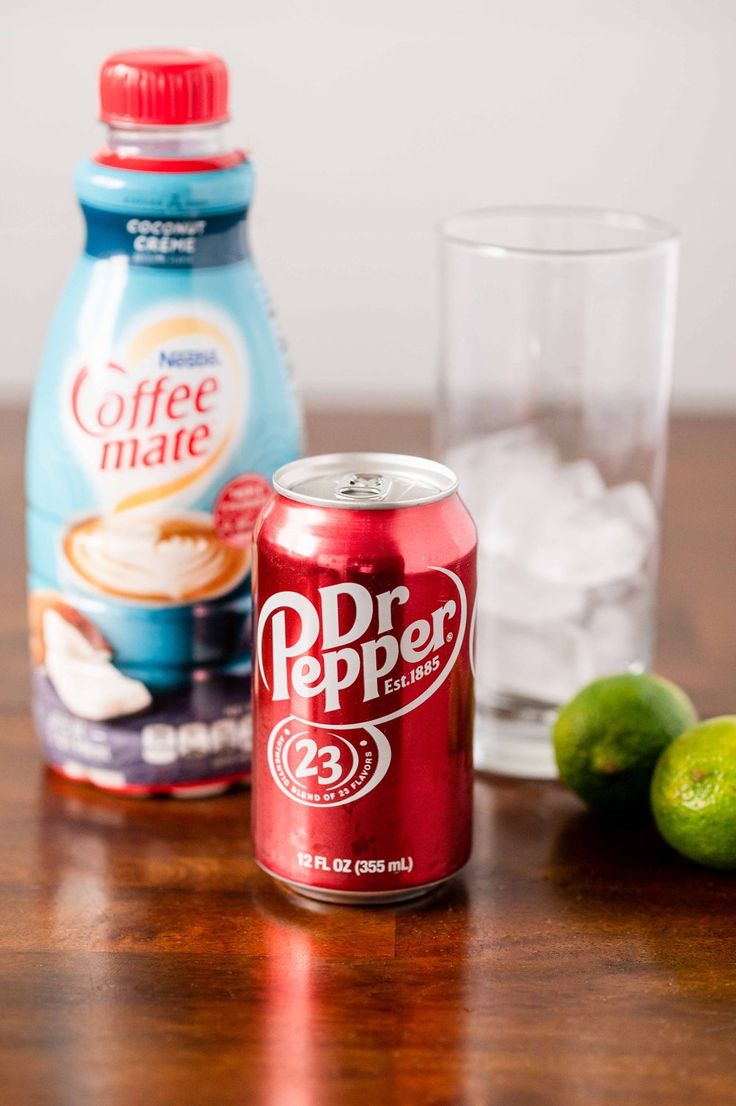 a can of dr pepper next to some limes and a glass on a table