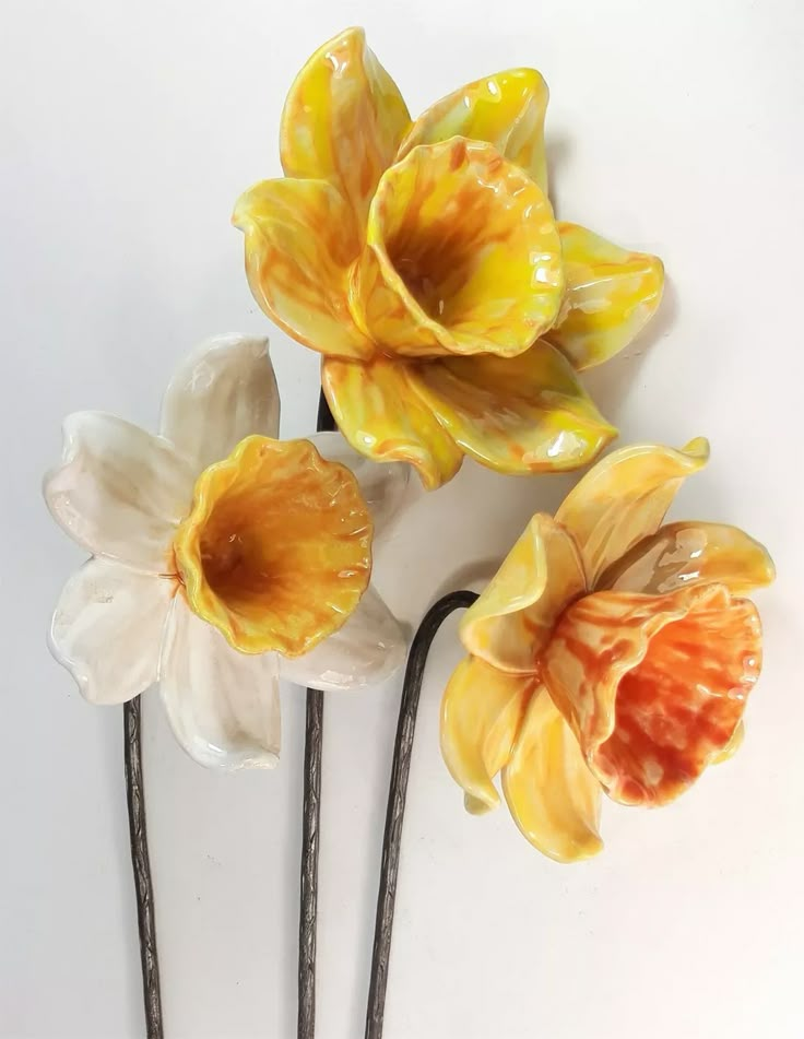 three yellow and white flowers sitting on top of each other next to two black sticks