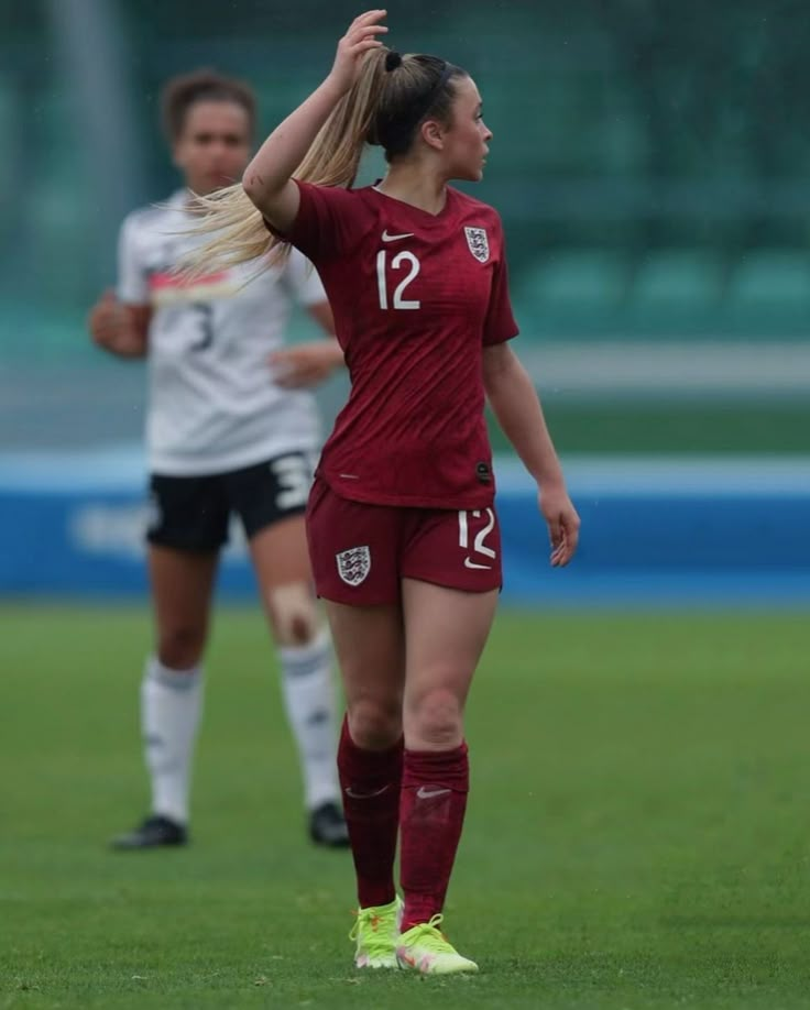 two female soccer players on the field during a game, one is holding her head up