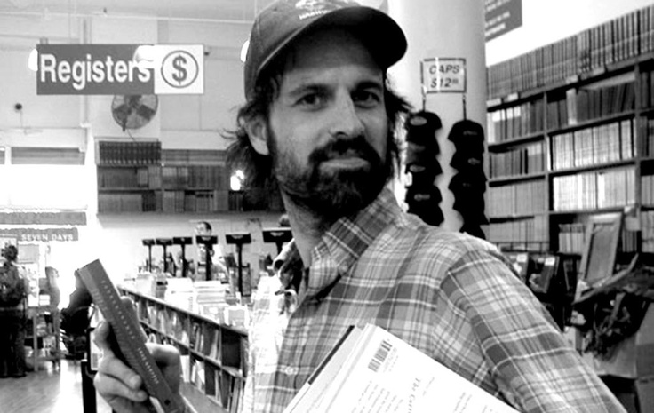 a man in a hat is holding a piece of paper and looking at the camera