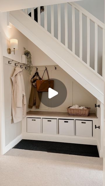 a hallway with white cabinets and drawers under a stair case next to a coat rack