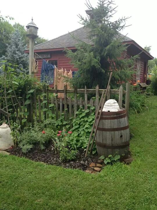 a wooden barrel sitting in the middle of a garden next to a fence with clothes hanging on it