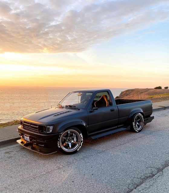 the truck is parked on the side of the road near the water and cliffs at sunset